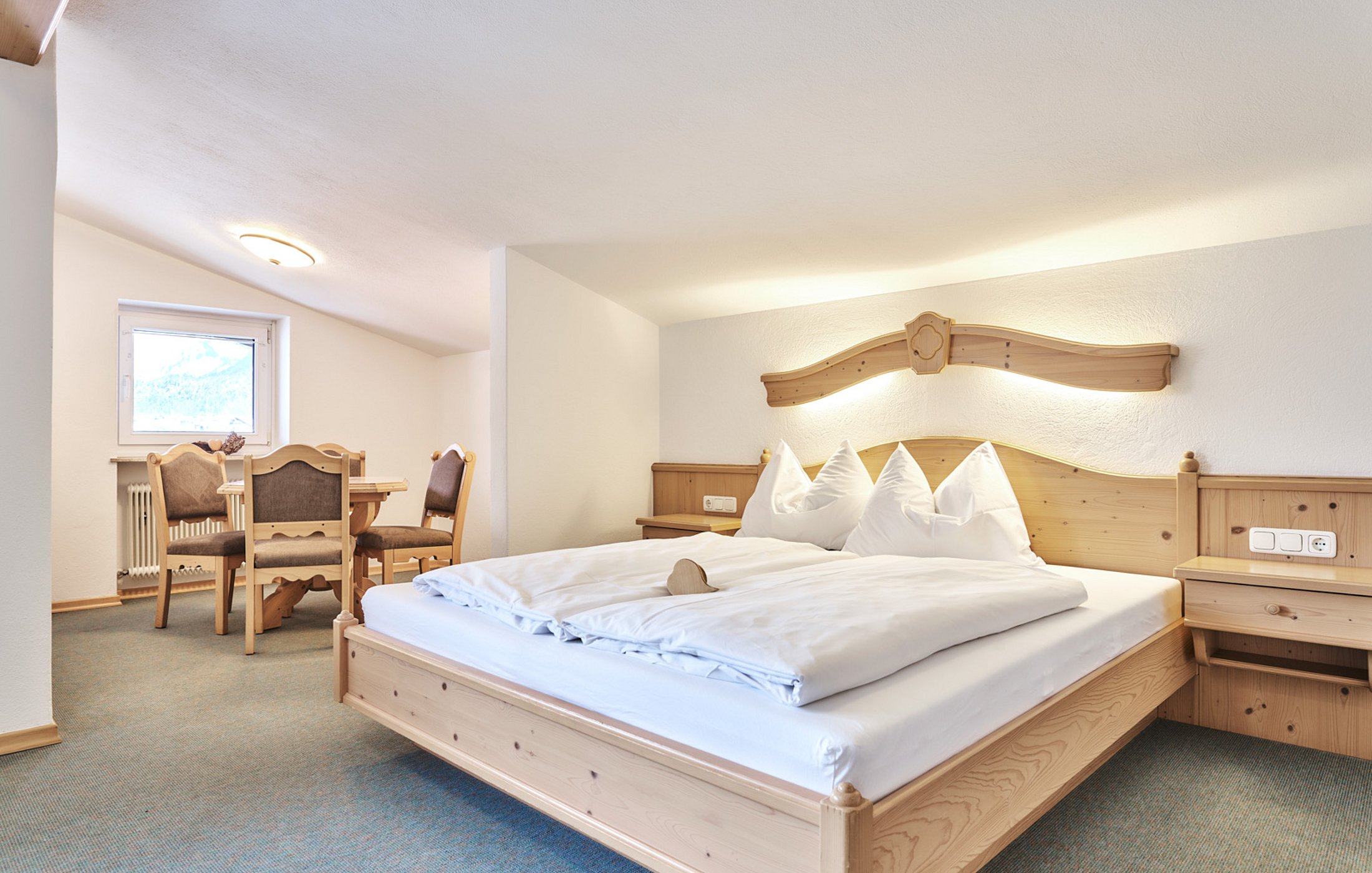 Helles Doppelzimmer mit Holzbetten, Nachttischen und Sitzbereich unter Dachschräge