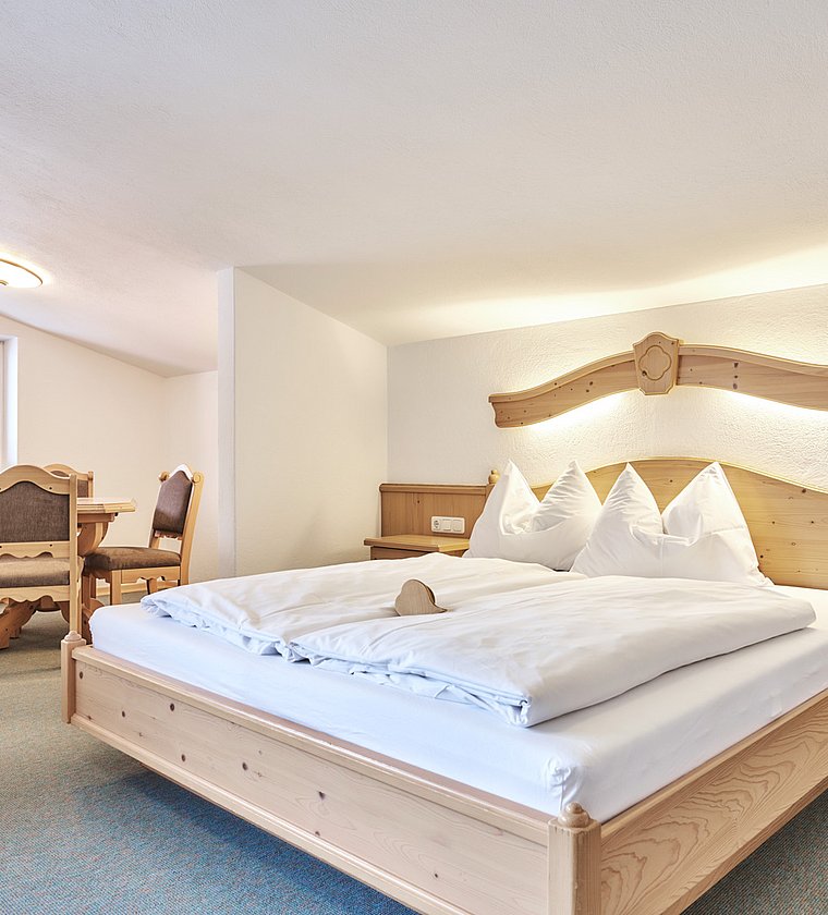 Bright double room with wooden beds, bedside tables and a seating area under the roof slope