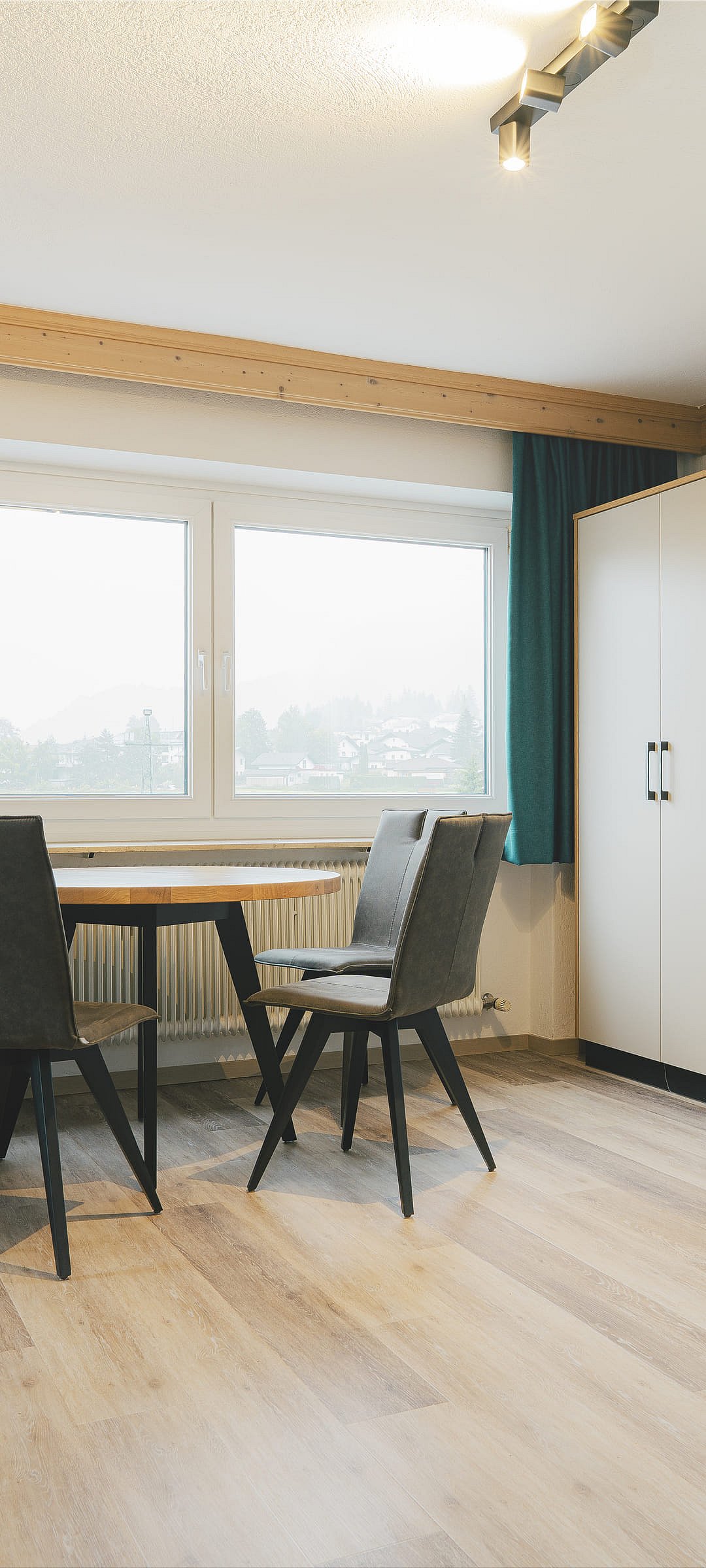 Living room in the holiday flat with a wooden table, sofa, wardrobe and green curtains