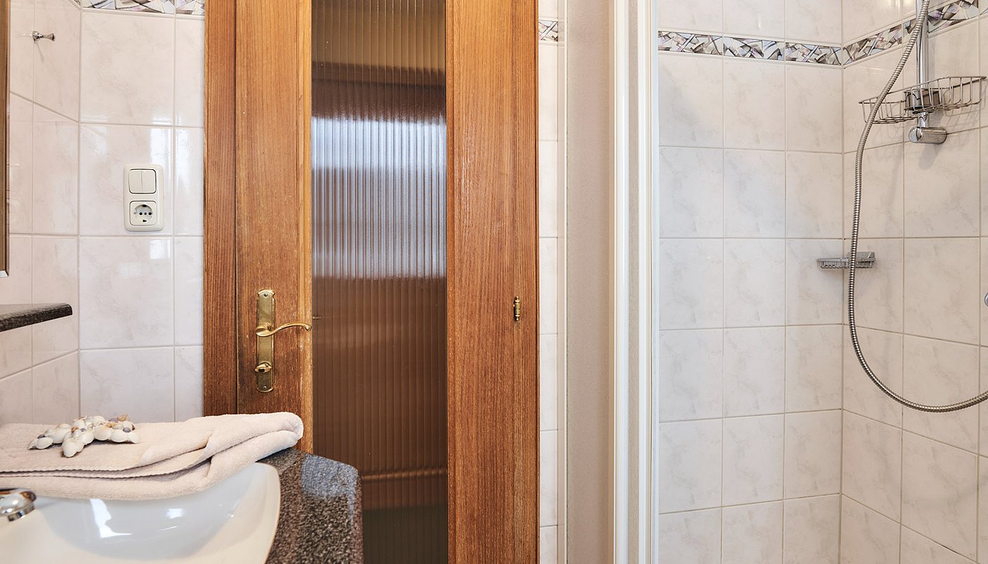 Sink with towels and decor, shower with handheld head and door with glass and wood frame