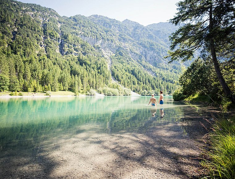 Man and woman wading in shallow Lake Heiterwang with mountain view