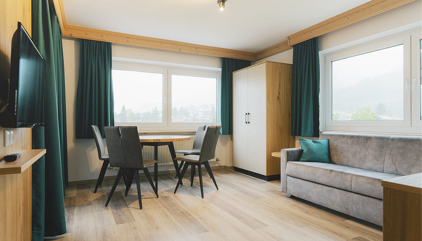 Living room in the holiday flat with a wooden table, sofa, wardrobe and green curtains