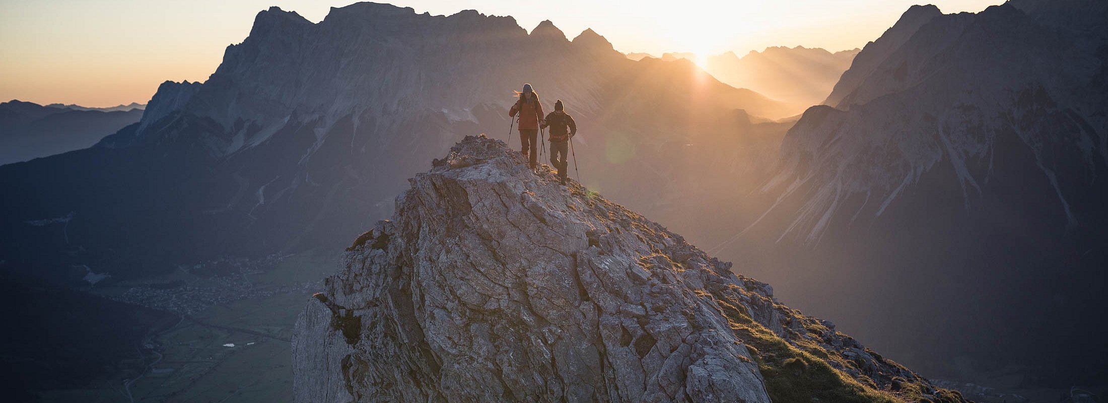 Two hikers on a mountain summit at sunrise with panoramic mountain view