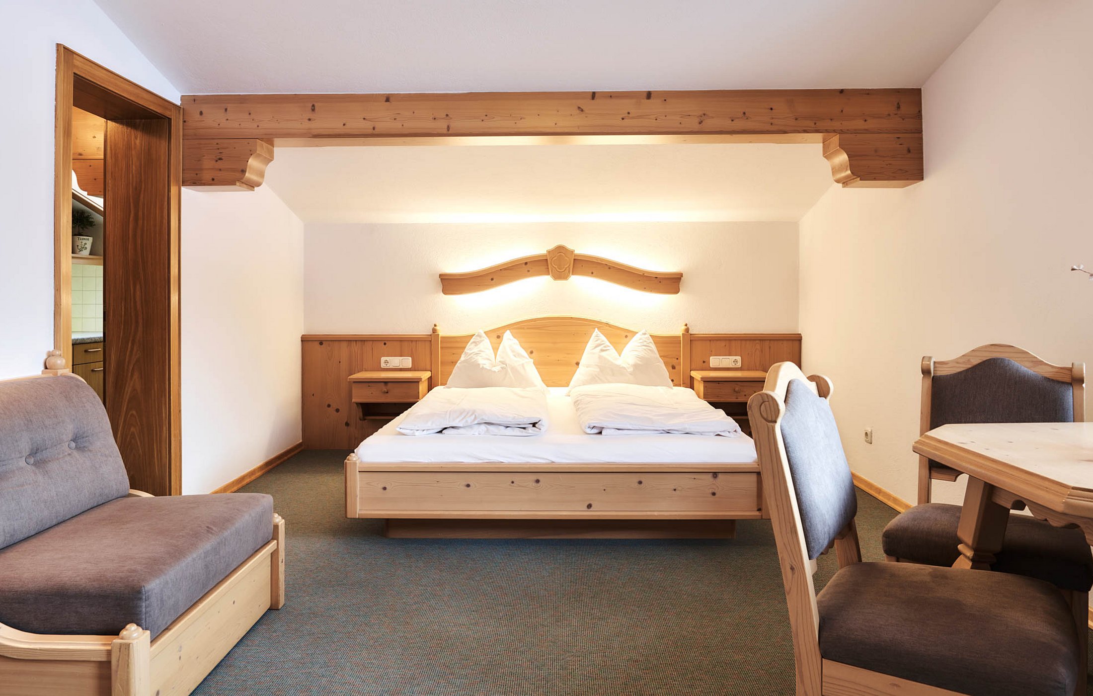 Alpine hotel room with double bed, seating area, and view into the kitchenette