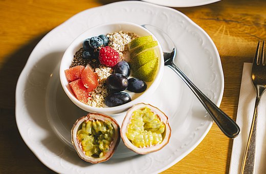 Bowl of yogurt with oats and fresh fruit such as berries, pear, and passion fruit on a plate