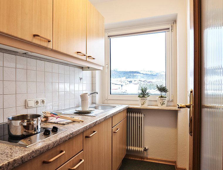 Functional kitchen with wooden cabinets, stovetop, sink and winter mountain view outside