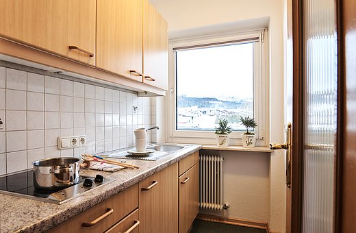 Functional kitchen with wooden cabinets, stovetop, sink and winter mountain view outside