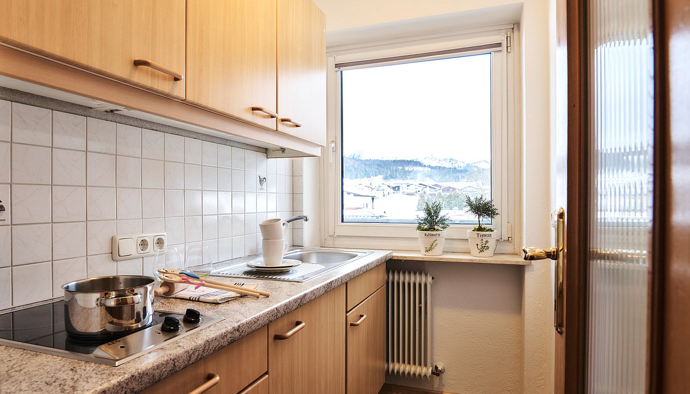 Functional kitchen with wooden cabinets, stovetop, sink and winter mountain view outside