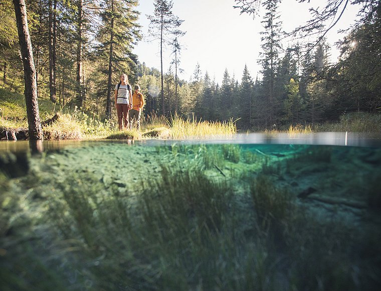 Hikers at a clear mountain lake in the forest, partially photographed underwater