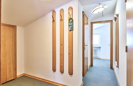 Hallway with wooden doors, three coat hooks and a view into a bright bedroom
