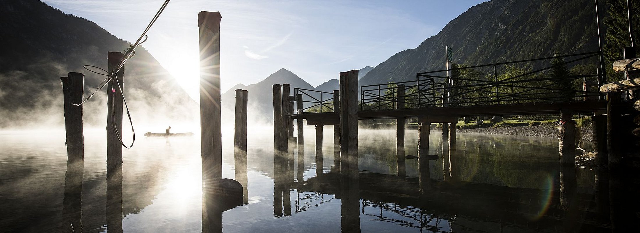 Morning sun at the pier on Lake Heiterwang with misty atmosphere and kayaker in the distance