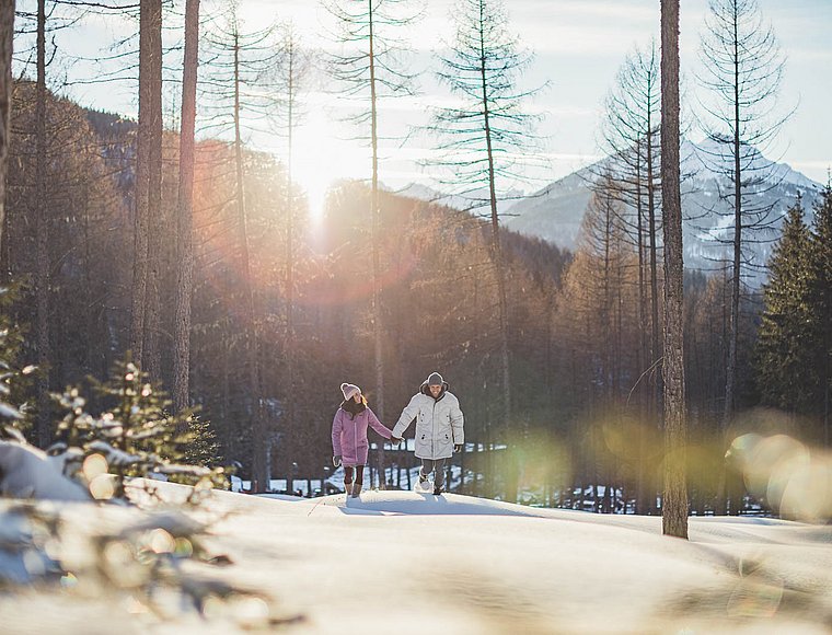 Couple walking through snowy forest at sunset with romantic light atmosphere