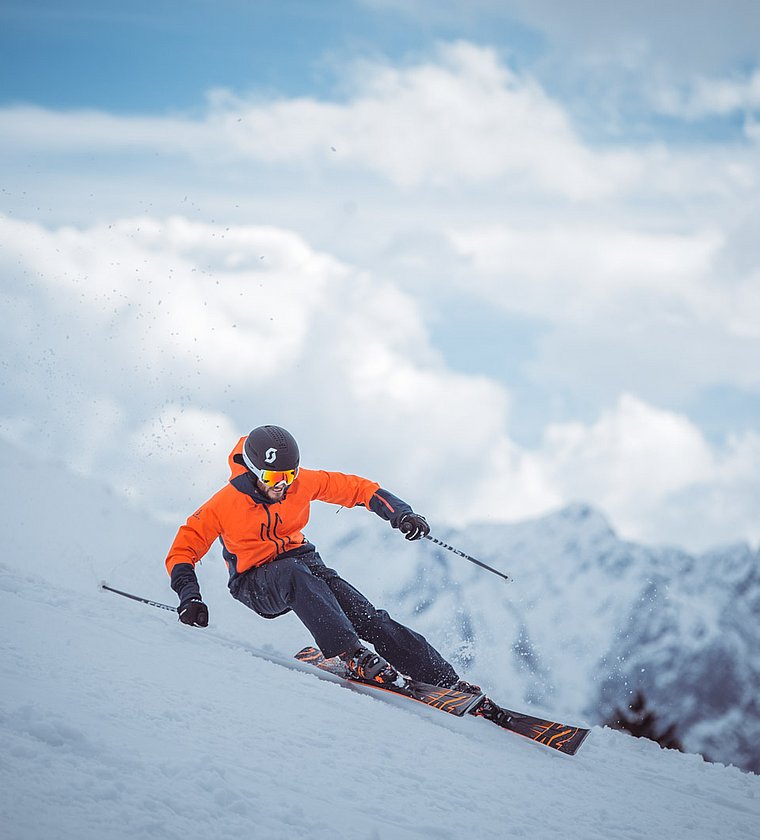 Skier in orange jacket carving a turn on a snowy mountain slope in the alpine landscape