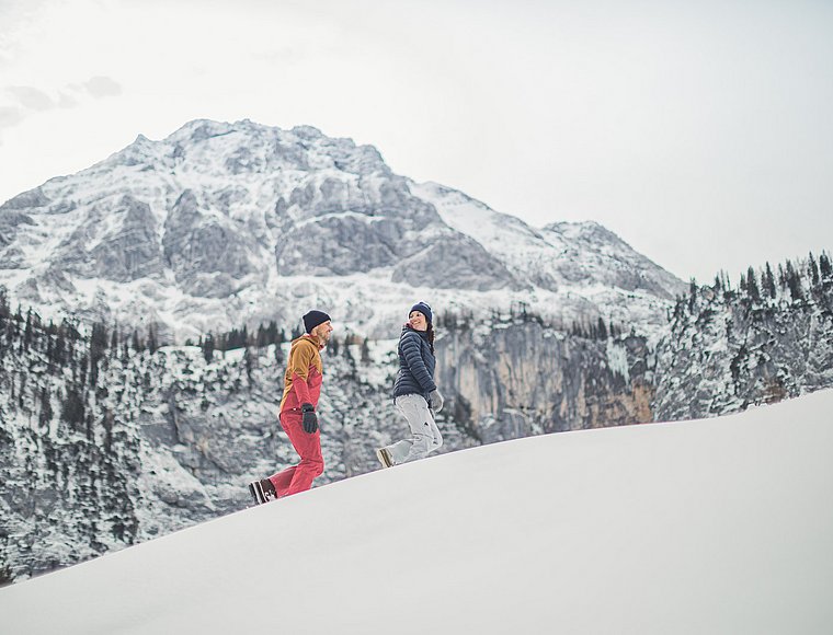 Couple winter hiking with snowy cliffs and majestic mountain panorama in the background