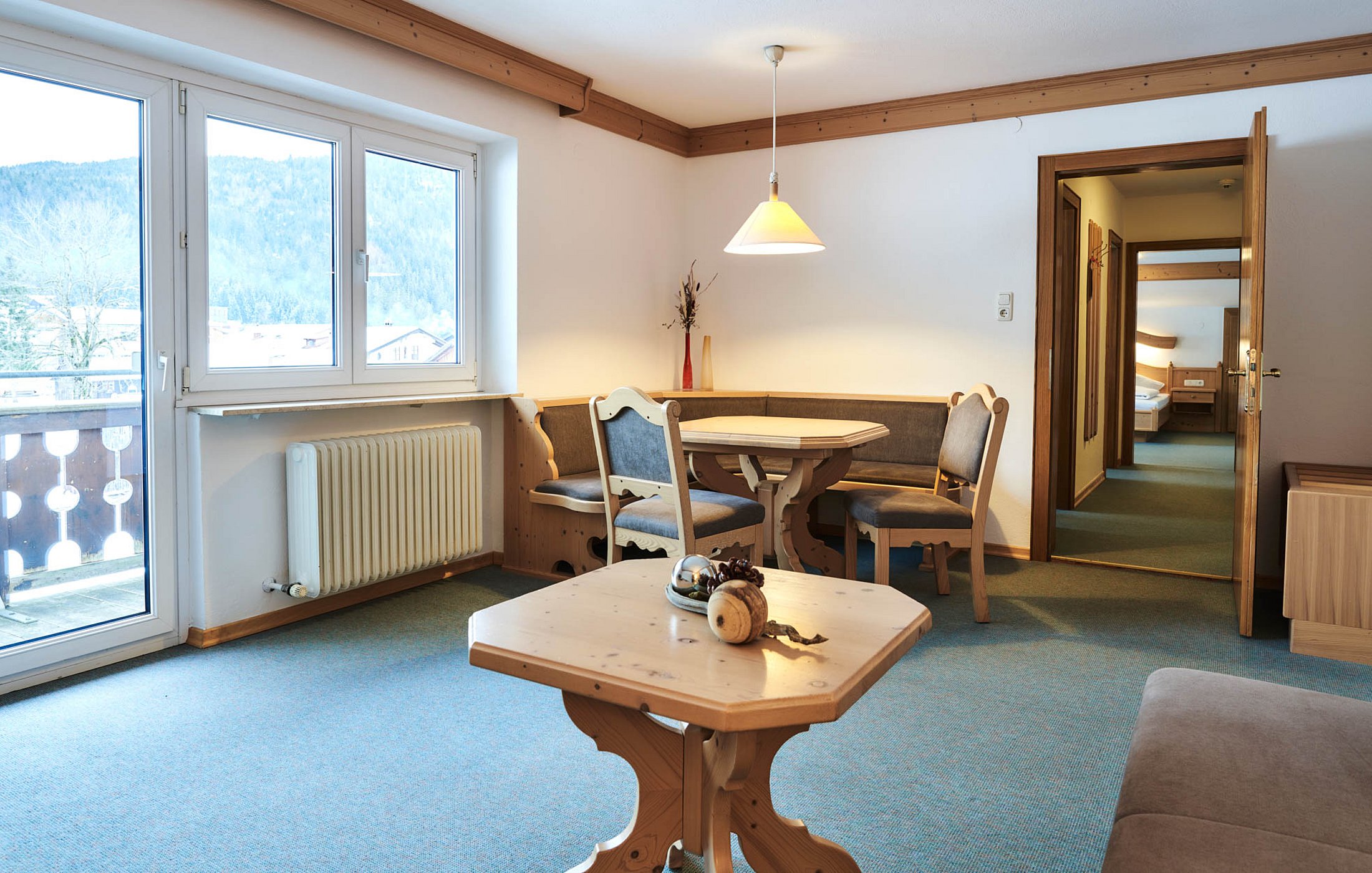 Dining area with corner bench and round table in hotel room with view into bedroom