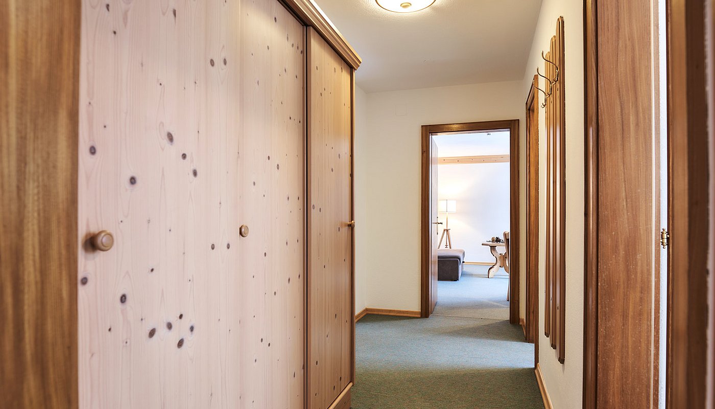 Long hallway with wooden cabinets and coat rack, view into cozy living or bedroom area