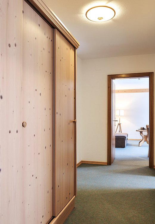 Long hallway with wooden cabinets and coat rack, view into cozy living or bedroom area