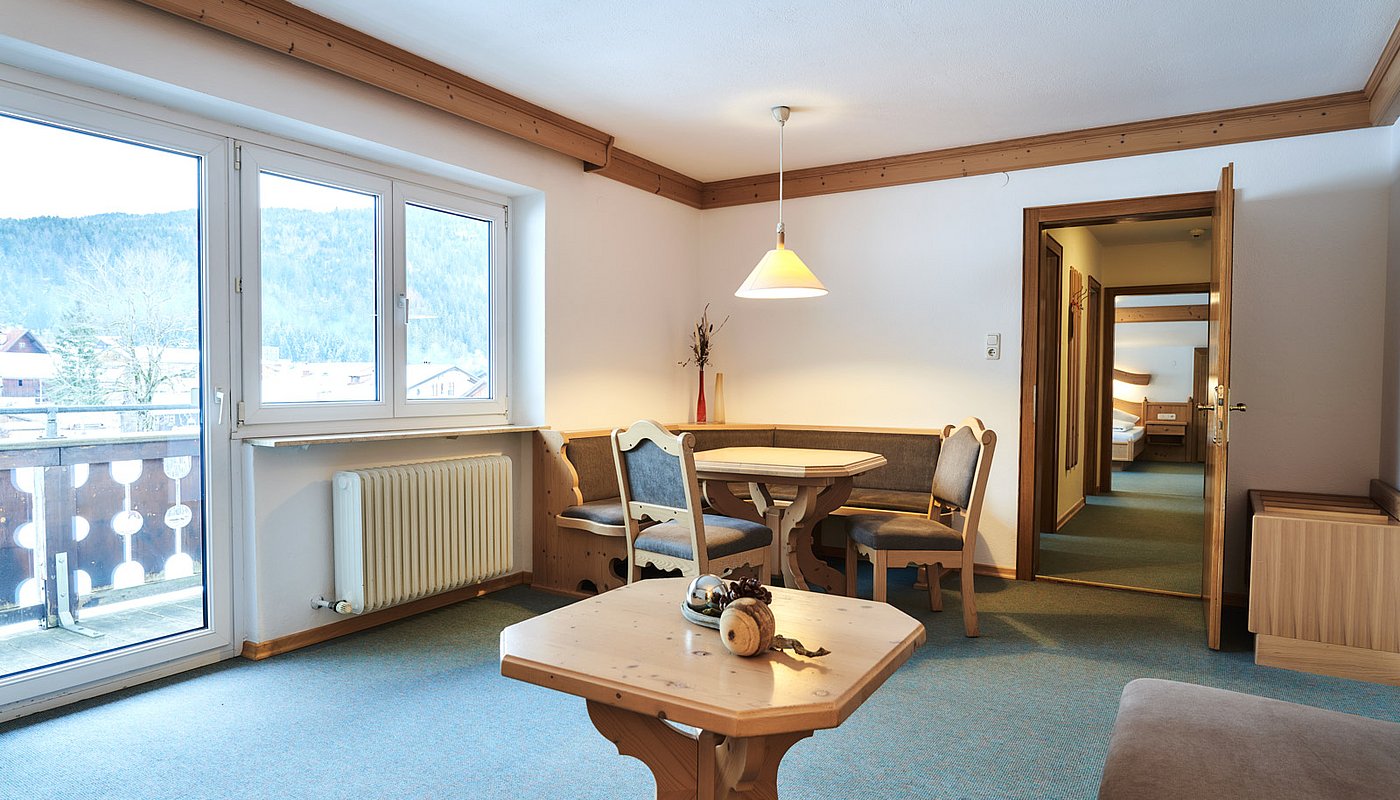 Bright dining area with wooden table, corner bench and mountain view through balcony door