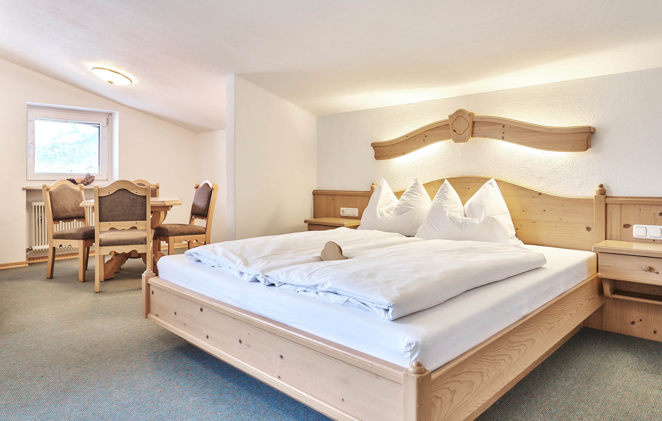 Cozy double bed and dining table in alpine-style hotel room with wooden décor