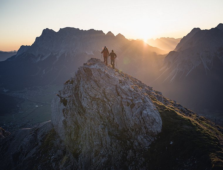 Two hikers on a summit at sunrise overlooking a stunning mountain panorama