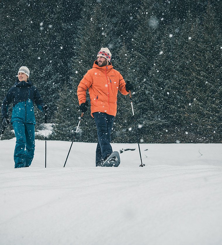 Couple snowshoe hiking in snowfall in front of fir forest