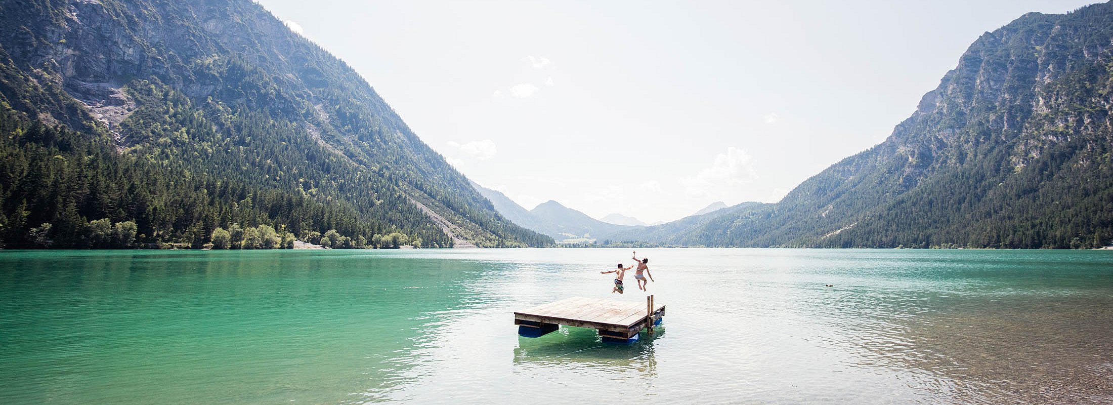 Two kids jump from platform into Lake Heiterwang on a sunny summer day
