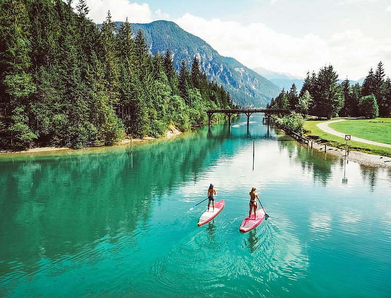 Two people stand-up paddling on turquoise water with a bridge in the background