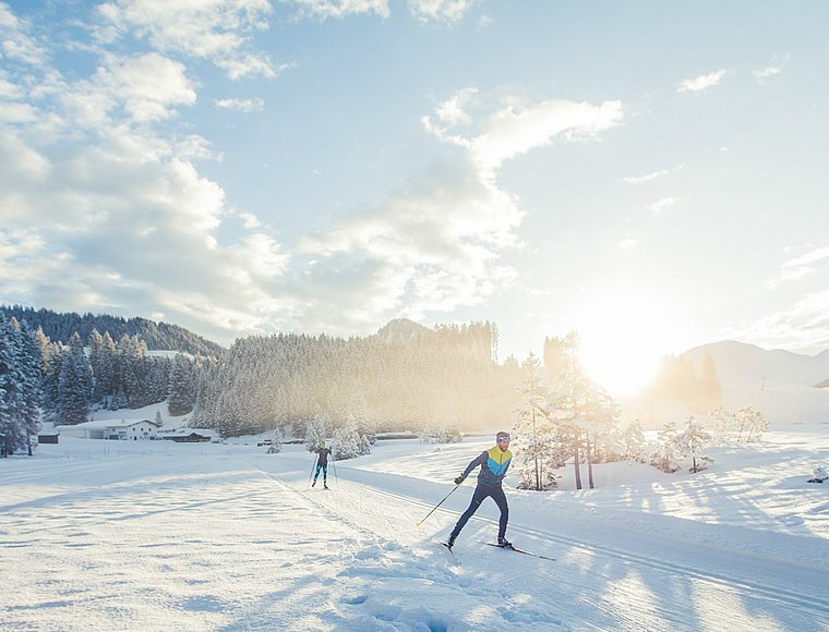 Cross-country skier in sunny winter landscape with wide open snowy trail