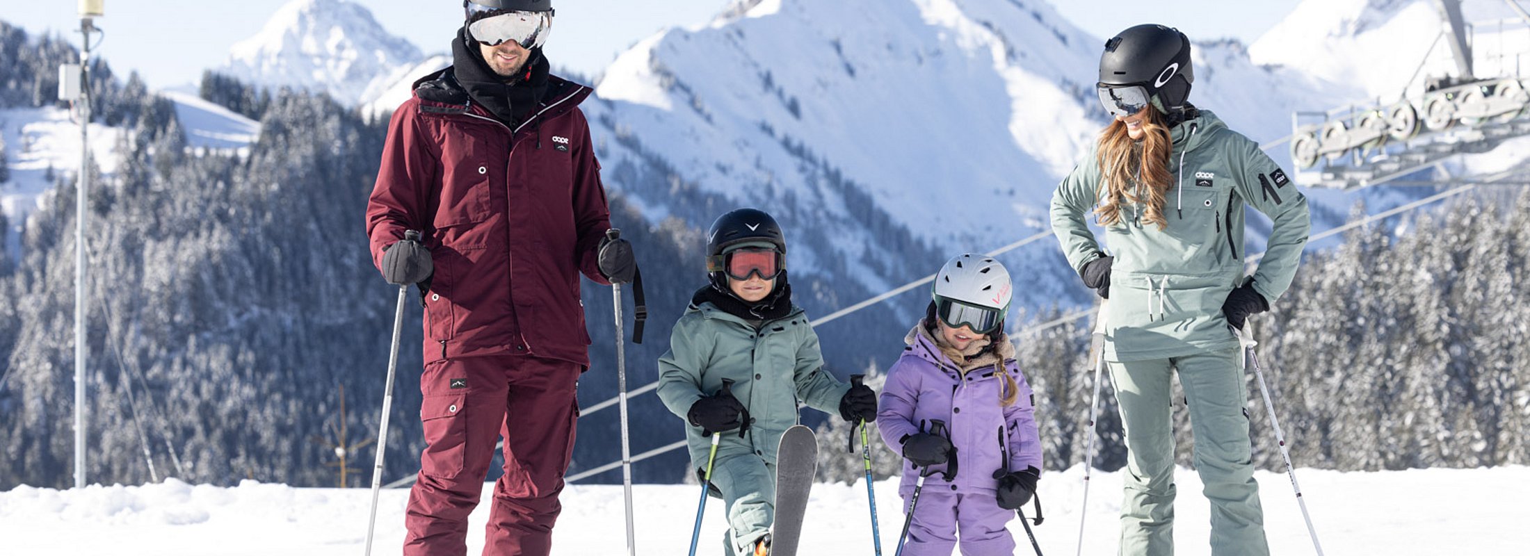 Skifamilie mit zwei Kindern vor verschneiten Bergen und Seilbahn